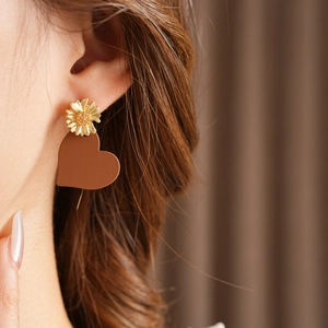 Close-up of asymmetrical gold flower and brown heart drop earrings on a model