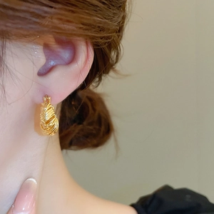 Close-up of gold U-shaped earrings with intricate woven texture on a female model