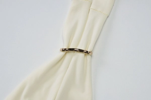 Close-up of a decorative gold metal ring detail on white knit fabric summer top