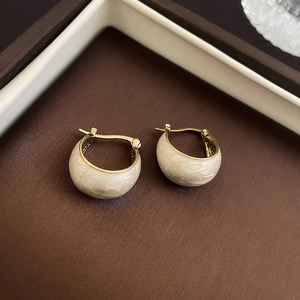 Macro shot of C-shaped golden earrings with creamy white marble pattern in a gift box