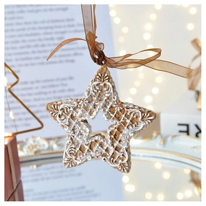 Close-up of a gingerbread star ornament with white icing hanging on a silk ribbon