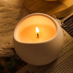 Candela profumata in ceramica bianca a forma di uovo su base in legno e sfondo accogliente