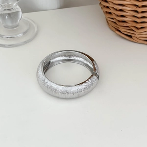 Detail shot of a silver metal cuff bracelet featuring a vertical striped texture on white surface