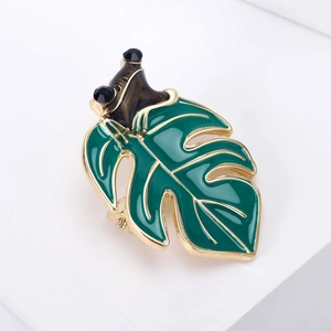 Detailed close-up of a green enamel monstera leaf brooch with a small black frog accent