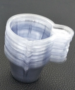 Stack of clear plastic measuring cups with small handles for resin mixing on leather