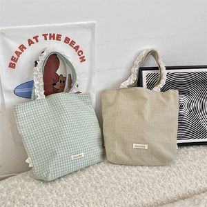 Detailed view of plaid canvas tote bags with delicate white lace trim on the handles