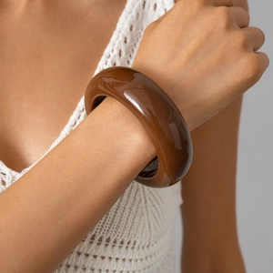 Close-up of a wide dark amber resin bangle on a wrist with a high-gloss finish