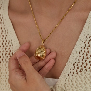 Macro detail of a gold drop-shaped pendant with shell texture on a twisted rope chain