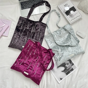 Flat lay of velvet tote bags with pearls, laptop and books on white fabric background