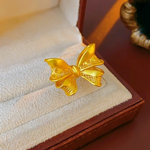 Detailed view of gold bow-knot ring with intricate filigree on beige velvet jewelry box