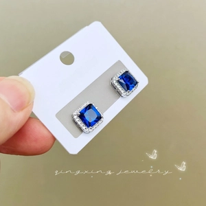 Close-up of square blue gemstone earrings with halo design on a jewelry card