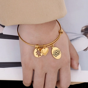 Adjustable gold bangle with delicate heart, girl and lotus flower charms on a model