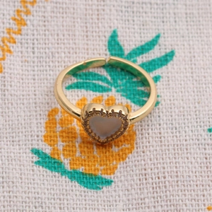 Detailansicht eines vergoldeten Herzrings mit Zirkonia-Inlay auf Ananas-Textilhintergrund