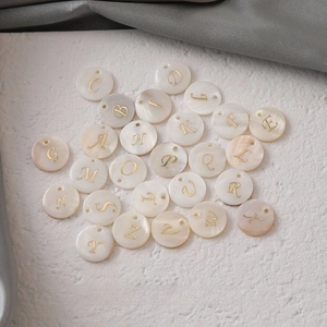 Macro shot of circular freshwater shell pendants with golden engraved letters for DIY jewelry