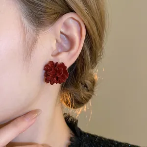 Elegant deep red ruffled flower stud earrings with glossy finish on model