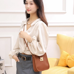 Sac bandoulière marron texture litchi avec fermoir doré porté par un mannequin chic
