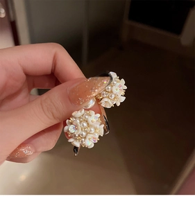 Detail of floral earrings with white resin petals and pearls held by hand in warm light