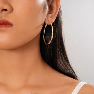 Gros plan de boucles d'oreilles créoles dorées au design torsadé sur un modèle