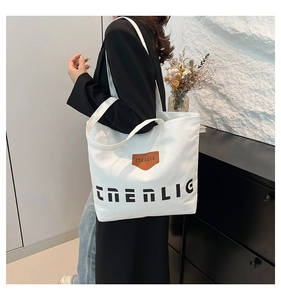 Close-up of white canvas tote bag with black letter print and brown leather brand tag