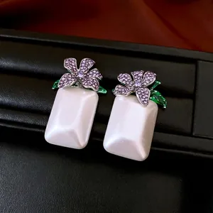 Ohrringe mit lila Kristallblumen und Perlen auf einem schwarzen Lederständer präsentiert
