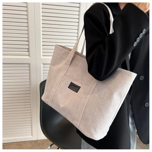 Detail of minimalist beige canvas tote bag with fashion label worn by a model