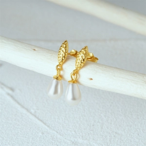 Macro detail of gold leaf earrings with white teardrop pearls on a minimalist white stand
