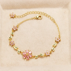 Detailed view of gold chain bracelet with pink crystal flowers and green leaf charms