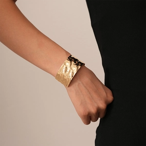 Detail of a wide gold metal cuff bracelet with textured crumpled surface worn by a model