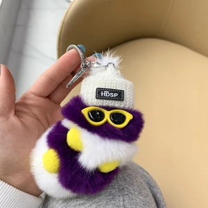 Detail of purple caterpillar plush keychain with a knitted hat and yellow glasses charm