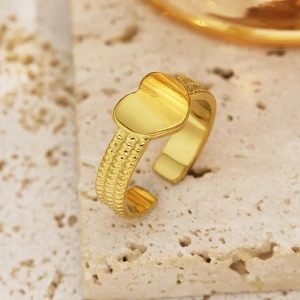 Vista macro de un anillo de corazón ajustable con banda dorada texturizada sobre mármol
