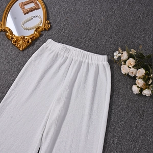 Vue détaillée du pantalon blanc plissé à jambes larges sur un fond sombre texturé avec décor
