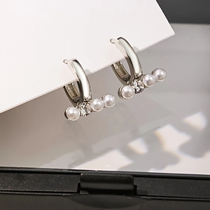 Détail de boucles d'oreilles argentées avec perles alignées et strass brillants
