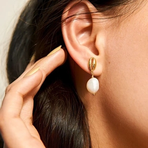 Fashionable golden shell earrings with irregular white pearls worn by a female model