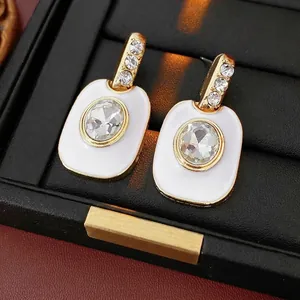 Boucles d'oreilles vintage en or avec émail blanc et cristaux dans une boîte à bijoux noire
