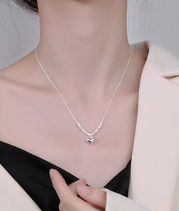 Close-up of a silver heart-shaped pendant necklace with beaded detail on a female model