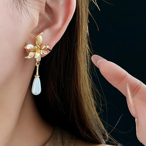 Macro detail of 14K gold plated flower earrings with elegant white teardrop pearl drops