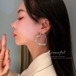 Boucles d'oreilles créoles cœur argentées avec strass brillants portées par un mannequin