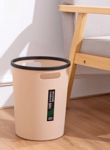 Detail of round beige trash bin with press ring and ergonomic handles in a modern living room