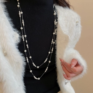 Detail of layered pearl necklace with silver flower charm on black sweater
