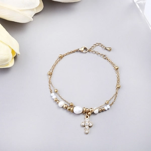 Detail of gold double-layer bracelet with pearls and a crystal-encrusted cross charm