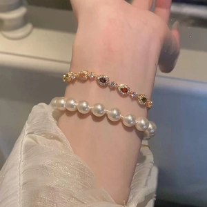 Detail of layered gold bracelet with pear-cut colorful zircons and white pearl band