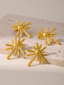 Detailed macro view of 18K gold-plated stainless steel sunburst stud earrings on a stone base