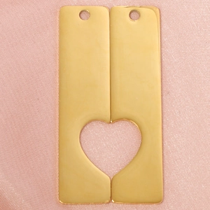 Detail of golden stainless steel rectangular pendants forming a hollow heart on pink fabric