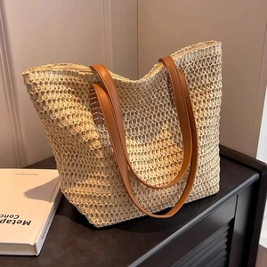 Detail of handwoven straw tote bag with brown leather straps and zipper closure