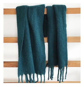 Detailed close-up of dark green knit scarf texture with fringe hanging on wood ladder