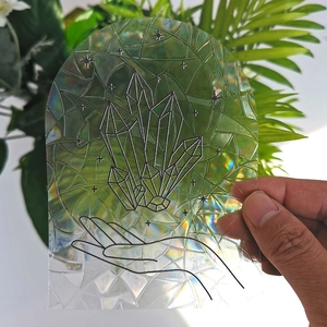 Close-up of holographic suncatcher sticker featuring crystal hand art on glass surface