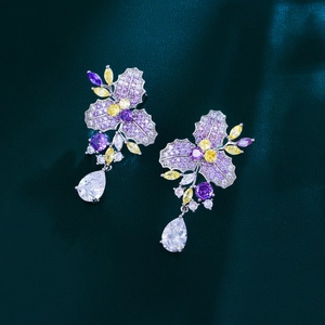 Luxurious flower drop earrings with purple and yellow zircon stones on dark green leather