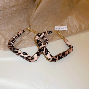Detail of leopard print faux leather hoop earrings with golden metal fasteners on paper