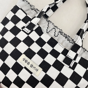 Detail of checkered canvas tote bag with white lace ruffle edge and Korean fabric label
