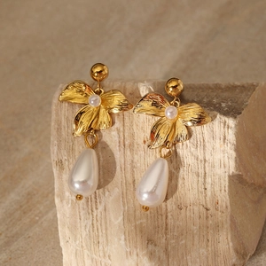 Detailed close-up of 3D gold flower earrings with a white pearl on a natural stone base